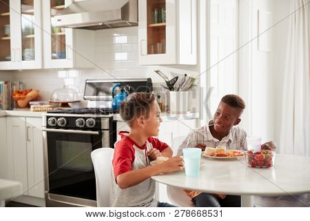 Two pre-teen male friends sit talking in the kitchen during a playdate at one boyÃs house