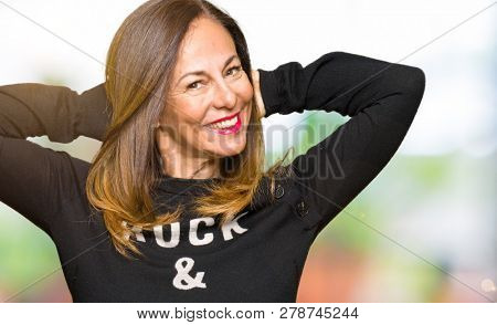Beautiful middle age woman wearing rock and roll sweater Relaxing and stretching with arms and hands behind head and neck, smiling happy