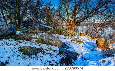 Beautiful Winter Landscape - View Of Forest On The River Bank With Trees, Large Stones And White Sno