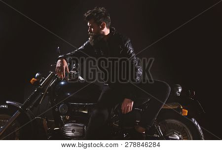 Man With Beard, Biker In Leather Jacket Lean On Motor Bike In Darkness, Black Background. Biker Cult