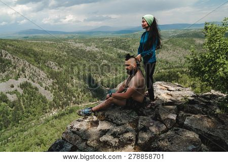 Asian Girl Doing Hair Style To Big Man On The Edge Of Rock In The Wild