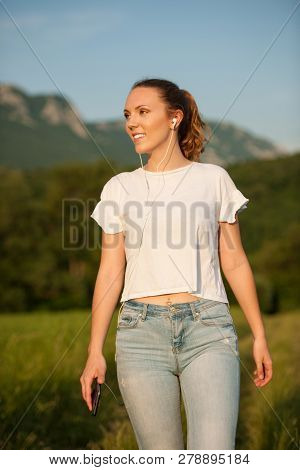 Beautiful Young Woman Walks On Meadow And Listen Music On Smart Phone