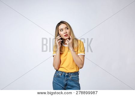 Portrait Of A Pensive Young Asian Woman Holding Mobile Phone And Looking Away Thinking Isolated Over