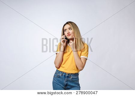 Portrait Of A Pensive Young Asian Woman Holding Mobile Phone And Looking Away Thinking Isolated Over