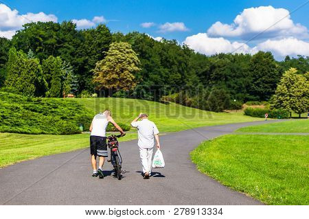 Poznan, Poland - July 29, 2018: Man With Shopping Bag Walking Next To Man With A Bicycle On A Footpa
