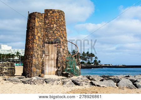 Stone Tower In Las Cucharas Beach, Lanzarote, Canary Islands. View Of The Sea, Sandy Beach And Rocks