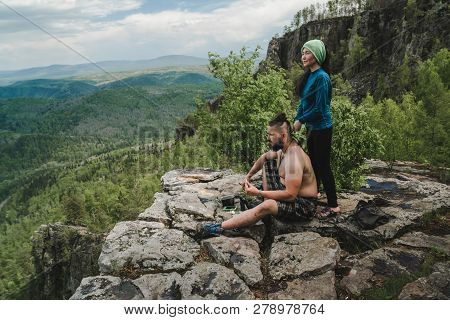 Asian Girl Doing Hair Style To Big Man On The Edge Of Rock In The Wild