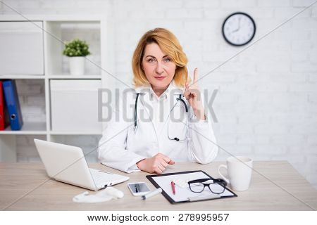 Potrtait Of Serious Mature Female Doctor Showing Attention Sign In Modern Office