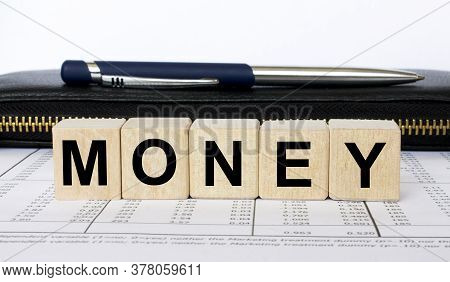 A Word Money Written In A Wooden Cube With A Pen And Purse