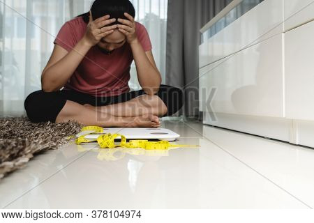 Weight Loss Fail Concept. Scale And Measure Tape With Depressed, Frustrated And Sad Woman Sitting On