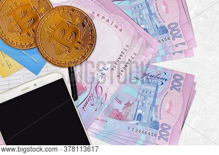 200 Ukrainian Hryvnias Bills And Golden Bitcoins With Smartphone And Credit Cards. Cryptocurrency In