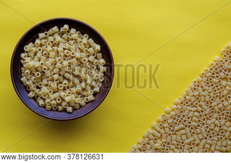 Clay Bowl With Ditalini Pasta On A Yellow Background. The Right Corner Is Occupied By Dry Ditalini. 