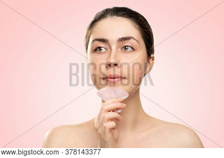 Gua Sha Massage. A Woman In A White Bath Towel Massages Her Chin With A Quartz Guasha Scraper. Pink 