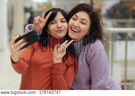 Two Young Women Taking Selfie With Victory Signs, Looking At Smart Phone Screen, Being Happy And Exp