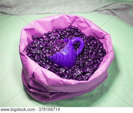 Lot Of Coffeebeans In A Paper Bag And A Purple Ceramic Cup