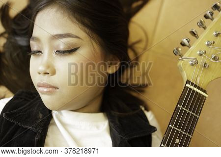 An Asian Girl Who Closes Her Eyes And Cries Near Her Electric Guitar.