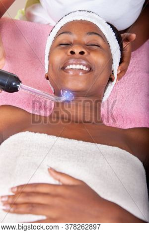 smiling young african woman having a laser face therapy in the hotel spa