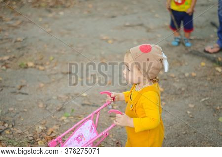 Photo Of A Toddler Girl In The Funny Hat Playing With A Toy Stroller