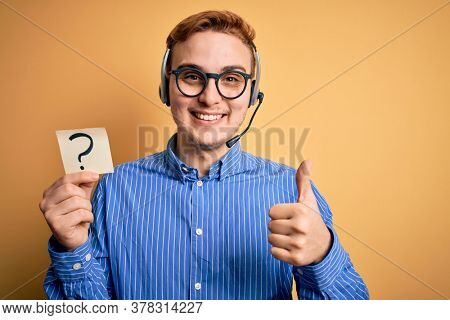 Redhead call center agent man working using headset holding reminder with question mark Smiling happy and positive, thumb up doing excellent and approval sign