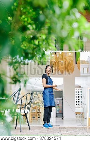 Happy Pretty Youg Black Woman Standing At Entrance Doors Of Her Cafe And Inving Customers Inside