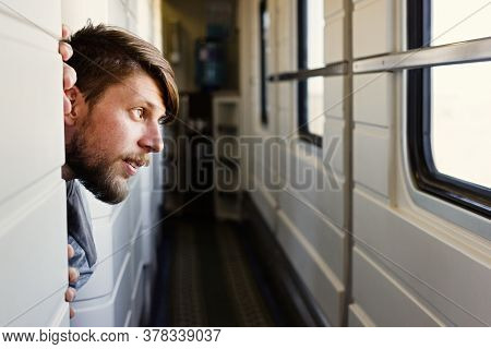 Handsome Young Caucasian Man With A Beard, Looks Outside Of The Trains Window, Looking At The Landsc