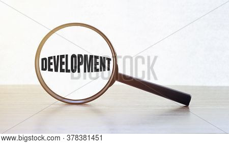 Magnifying Glass With Text Development On Wooden Table.