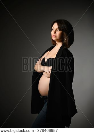 Brunette Pregnant Female In Black Shawl, Pants And Bra, Bare Belly. She Looking Aside, Hands Folded,