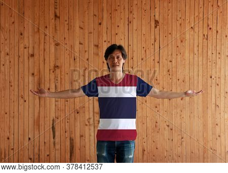 Man Wearing Thailand Flag Color Shirt And Standing With Arms Wide Open On The Wooden Wall Background