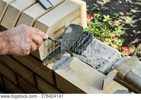 Bricklayer Installing Bricks On The New Fence From Facing Bricks Using Putty Knife.