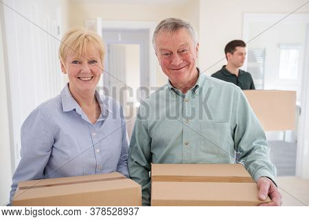 Portrait Of Senior Couple Downsizing In Retirement Carrying Boxes Into New Home On Moving Day With R