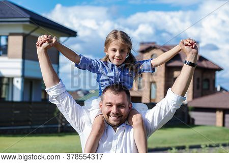Photo Of Dad Holding His Little Daughter With Love On His Shoulders Against The Background Of His Ne