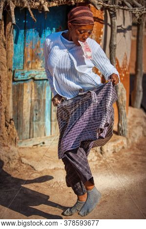 african woman dancing holding a twenty pula note in her mouth in front of her house