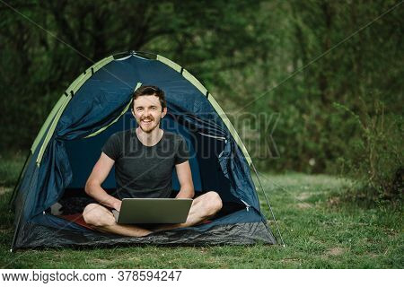 Man Working On Laptop In Tent In Nature. Young Freelancer Sitting In Camp. Relaxing In Camping Site 
