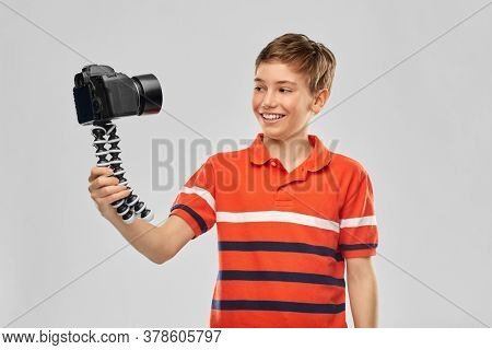 blogging, videoblog and people concept - portrait of happy smiling boy video blogger with camera and tripod videoblogging over grey background