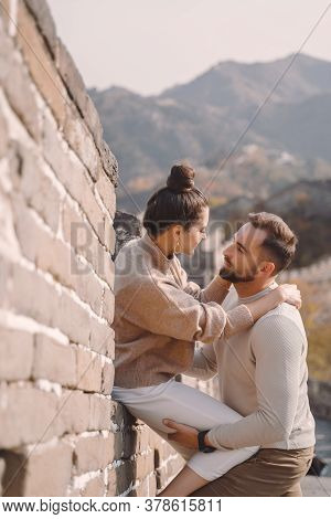 Beautiful Young Couple Sitting Down And Showing Affection At The Great Wall Of China.