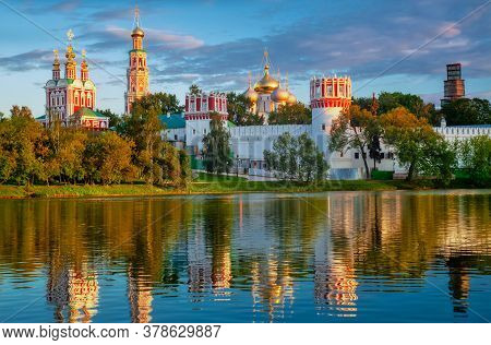 Novodevichy Monastery With A Reflection In The Lake At Sunset. The Famous Moscow Landmark With Golde