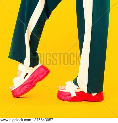 Women's Legs In Sport Sandals With Red Soles And Green Pants With Stripes On A Yellow Background.
