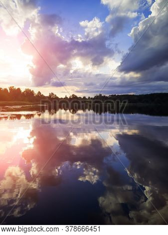 Summer Landscape: The Sky With Clouds And The Forest On The Horizon Are Reflected In The Clear Water