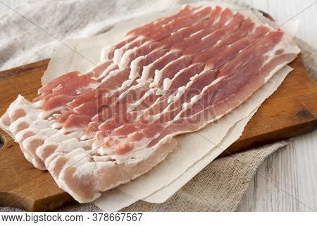 Uncooked Raw Bacon On A Rustic Wooden Board On A White Wooden Background, Side View. Close-up.