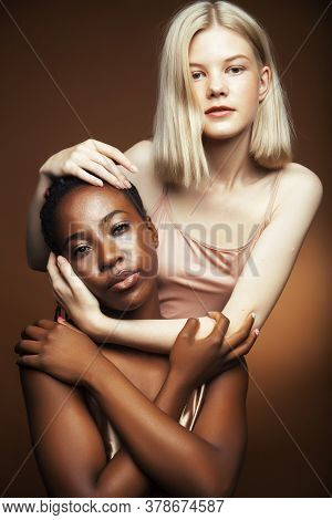 Two Pretty Girls African And Caucasian Blond Posing Cheerful Together On Browm Background, Etnithity