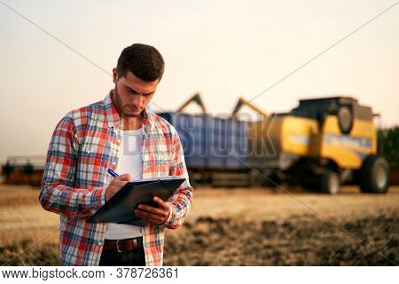 Farmer Controls Loading Wheat From Harvester To Grain Truck. Driver Holding Clipboard, Keeping Notes