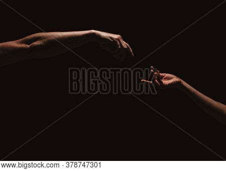Two Male Hands Reaching Out To One Another, Almost Touching, In Front Of Dark Clear Empty Background