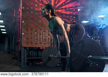 Side View Of Srtong Woman With Muscular Body In Sportswear Training Legs In Gym In Dark Atmosphere, 