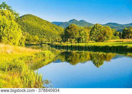 Croatia, River Gacka Flowing Between The Meadow Fields In Lika Region, Beautiful Green Nature