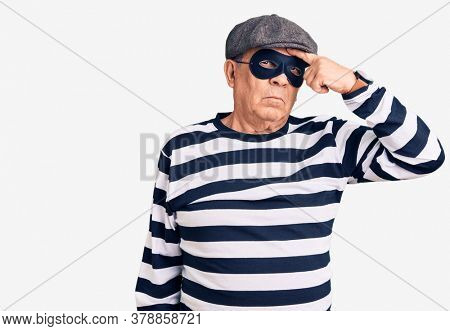 Senior handsome man wearing burglar mask and t-shirt pointing unhappy to pimple on forehead, ugly infection of blackhead. acne and skin problem 