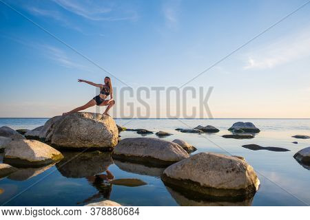 Full body young woman in underwear doing Skandasana pose on rock against sunset sky while doing yoga near peaceful sea in evening