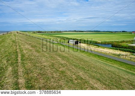 Typical Dutch View Of A Dike With Sheeps Overlooking The Polder With Farms, Green Grassland And The 