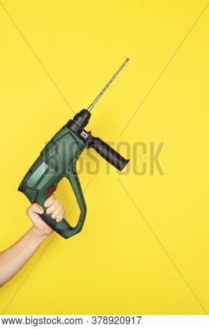 Green Puncher In The Hands Of A Builder. Female Hand Hold New Puncher Or Drill Isolated On Yellow Ba