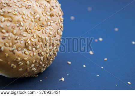 Part Of A Bakery Product Sprinkled With Sesame On The Left On A Blue Background