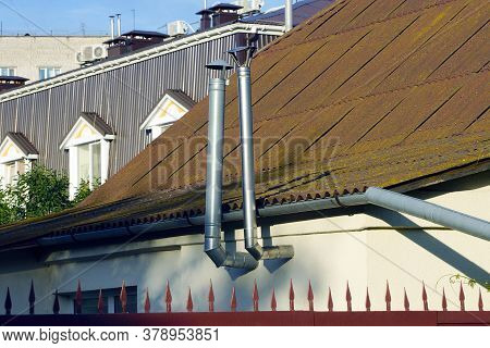 Two Gray Metal Chimney Pipes On The Wall Of The House Near The Brown Slate Roof